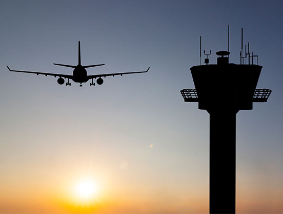 Aeroplane in the sky next to an Air Traffic Control Tower.