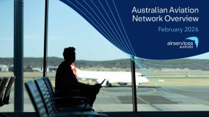 A man overlooks an airport runway and a stationary plane against a blue backdrop