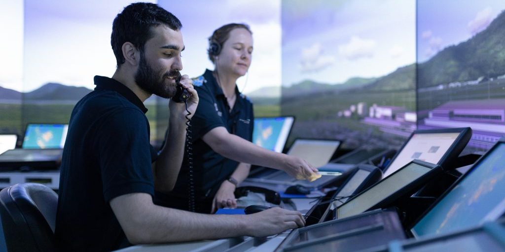 An ATC trainee and instructor in the Tower SIM against a simulated sky and trees