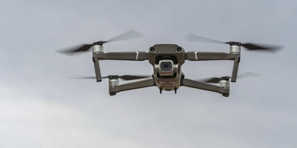A small quadcopter is flying at a low altitude against a gray sky and the camera is aimed at the photographer.