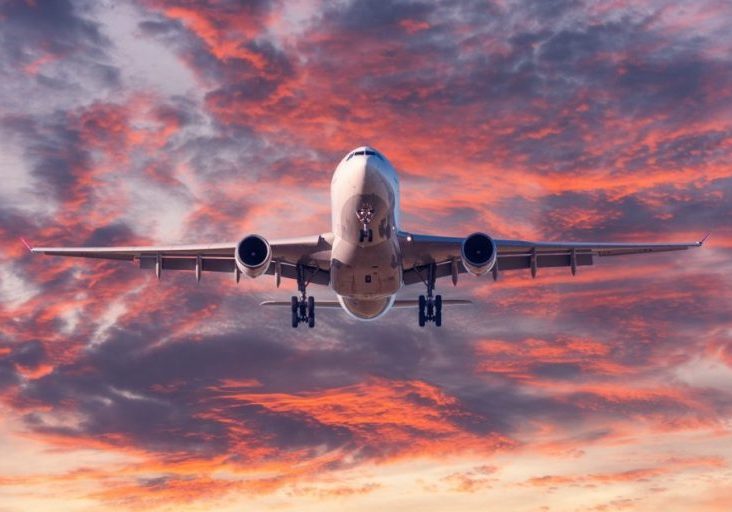Landing airplane. Landscape with passenger airplane is flying in the blue sky with red, purple and orange clouds at sunset. Travel background. Passenger plane. Commercial aircraft. Private jet
