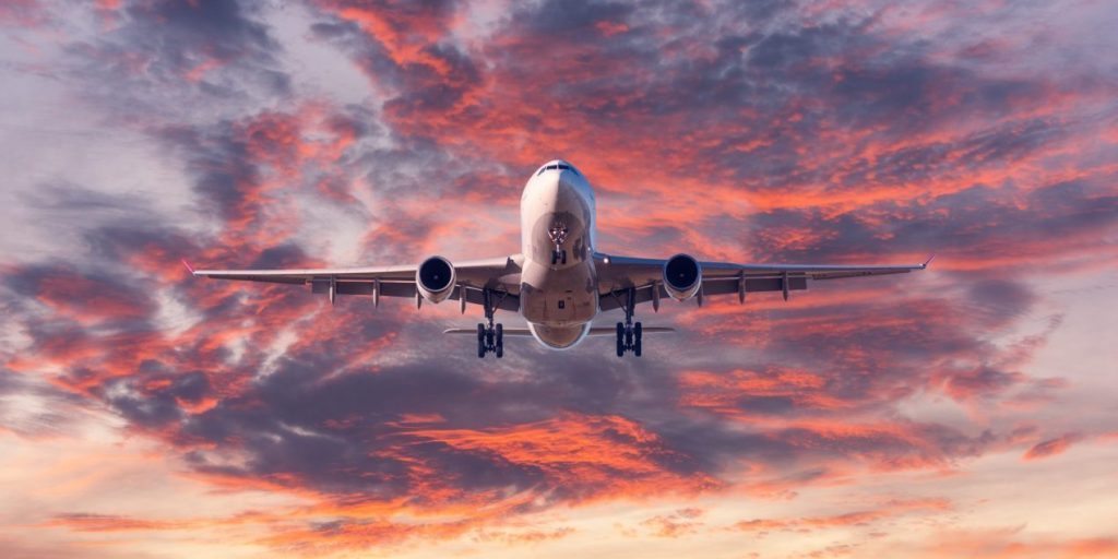 Landing airplane. Landscape with passenger airplane is flying in the blue sky with red, purple and orange clouds at sunset. Travel background. Passenger plane. Commercial aircraft. Private jet