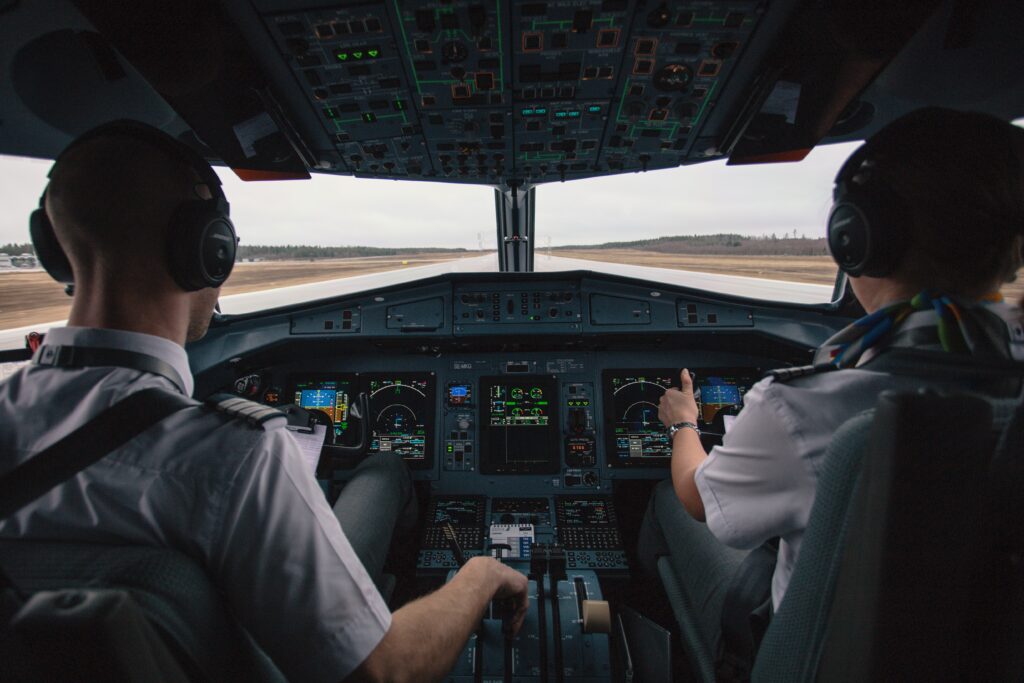 Two pilots in cock pit flying about to take off from tarmac.