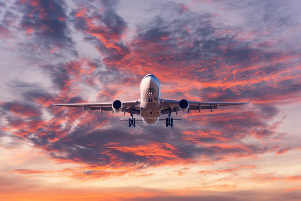 Landing airplane. Landscape with passenger airplane is flying in the blue sky with red, purple and orange clouds at sunset. Travel background. Passenger plane. Commercial aircraft. Private jet