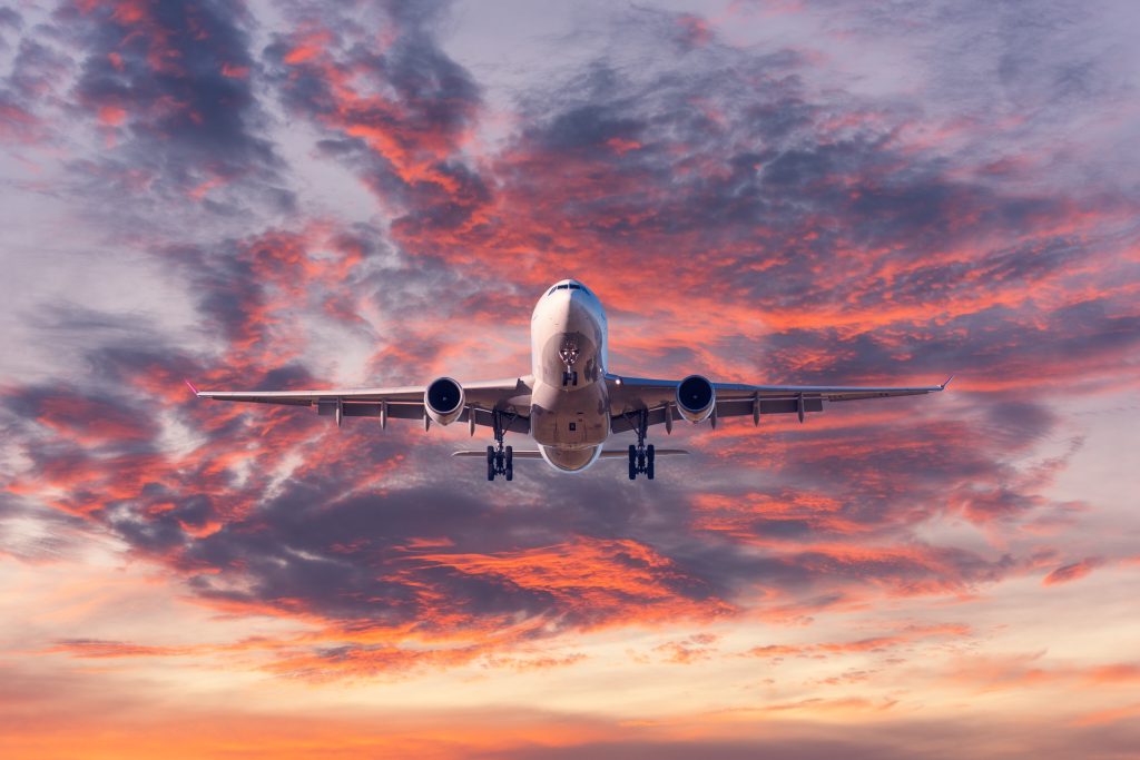 Landing passenger airplane at colorful sunset Landing airplane. Landscape with passenger airplane is flying in the blue sky with red, purple and orange clouds at sunset. Travel background. Passenger plane. Commercial aircraft. Private jet